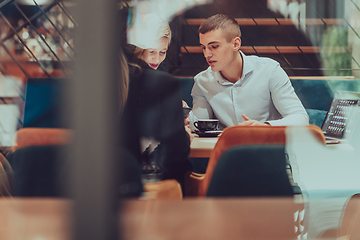 Image showing Photo through the glass of a group of business people sitting in a cafe and discussing business plans and ideas for new online commercial services