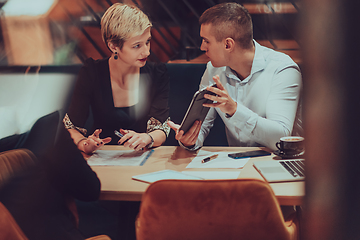 Image showing Photo through the glass of a group of business people sitting in a cafe and discussing business plans and ideas for new online commercial services