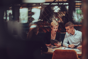 Image showing Photo through the glass of a group of business people sitting in a cafe and discussing business plans and ideas for new online commercial services