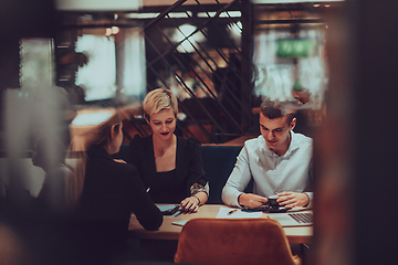 Image showing Photo through the glass of a group of business people sitting in a cafe and discussing business plans and ideas for new online commercial services