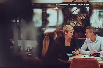 Image showing Photo through the glass of a group of business people sitting in a cafe and discussing business plans and ideas for new online commercial services