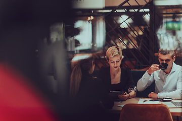 Image showing Photo through the glass of a group of business people sitting in a cafe and discussing business plans and ideas for new online commercial services