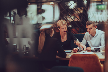 Image showing Photo through the glass of a group of business people sitting in a cafe and discussing business plans and ideas for new online commercial services