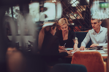 Image showing Photo through the glass of a group of business people sitting in a cafe and discussing business plans and ideas for new online commercial services