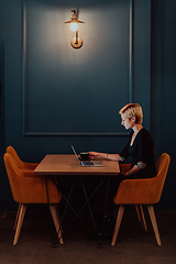 Image showing Businesswoman sitting in a cafe while focused on working on a laptop and participating in an online meetings. Selective focus.