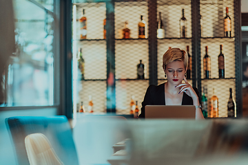 Image showing Businesswoman sitting in a cafe while focused on working on a laptop and participating in an online meetings. Selective focus.