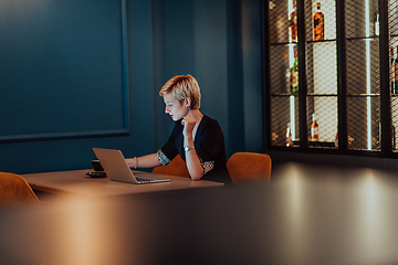 Image showing Businesswoman sitting in a cafe while focused on working on a laptop and participating in an online meetings. Selective focus.