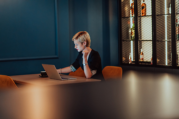 Image showing Businesswoman sitting in a cafe while focused on working on a laptop and participating in an online meetings. Selective focus.