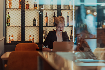 Image showing Businesswoman sitting in a cafe while focused on working on a laptop and participating in an online meetings. Selective focus.