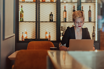 Image showing Businesswoman sitting in a cafe while focused on working on a laptop and participating in an online meetings. Selective focus.