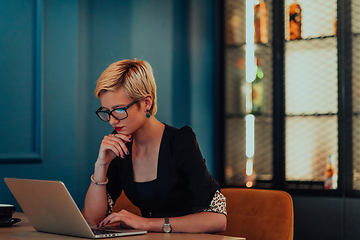 Image showing Businesswoman sitting in a cafe while focused on working on a laptop and participating in an online meetings. Selective focus.