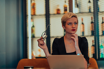 Image showing Businesswoman sitting in a cafe while focused on working on a laptop and participating in an online meetings. Selective focus.