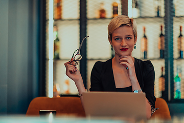 Image showing Businesswoman sitting in a cafe while focused on working on a laptop and participating in an online meetings. Selective focus.