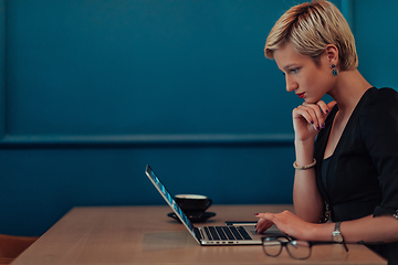 Image showing Businesswoman sitting in a cafe while focused on working on a laptop and participating in an online meetings. Selective focus.