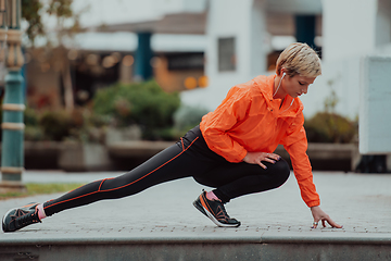 Image showing Fit attractive woman in sportswear stretching one leg before jogging on the footpath outdoor in summer among greenery. Workout, sport, activity, fitness, vacation and training concept.