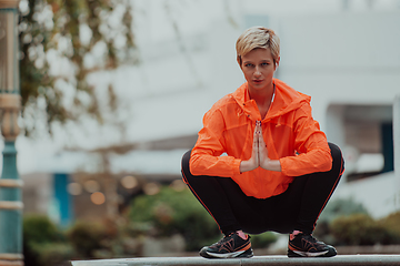 Image showing Fit attractive woman in sportswear stretching one leg before jogging on the footpath outdoor in summer among greenery. Workout, sport, activity, fitness, vacation and training concept.