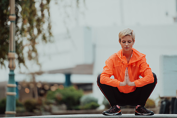 Image showing Fit attractive woman in sportswear stretching one leg before jogging on the footpath outdoor in summer among greenery. Workout, sport, activity, fitness, vacation and training concept.