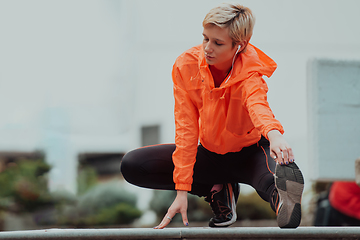 Image showing Fit attractive woman in sportswear stretching one leg before jogging on the footpath outdoor in summer among greenery. Workout, sport, activity, fitness, vacation and training concept.