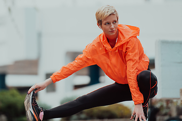 Image showing Fit attractive woman in sportswear stretching one leg before jogging on the footpath outdoor in summer among greenery. Workout, sport, activity, fitness, vacation and training concept.