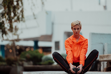 Image showing Fit attractive woman in sportswear stretching one leg before jogging on the footpath outdoor in summer among greenery. Workout, sport, activity, fitness, vacation and training concept.