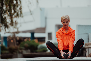 Image showing Fit attractive woman in sportswear stretching one leg before jogging on the footpath outdoor in summer among greenery. Workout, sport, activity, fitness, vacation and training concept.