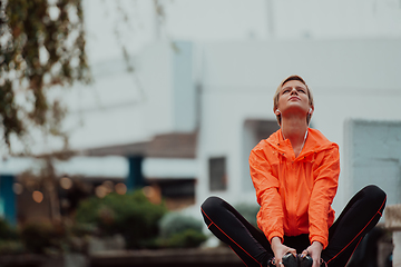 Image showing Fit attractive woman in sportswear stretching one leg before jogging on the footpath outdoor in summer among greenery. Workout, sport, activity, fitness, vacation and training concept.