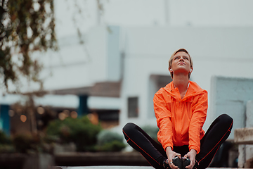 Image showing Fit attractive woman in sportswear stretching one leg before jogging on the footpath outdoor in summer among greenery. Workout, sport, activity, fitness, vacation and training concept.