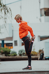 Image showing Fit attractive woman in sportswear stretching one leg before jogging on the footpath outdoor in summer among greenery. Workout, sport, activity, fitness, vacation and training concept.