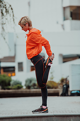 Image showing Fit attractive woman in sportswear stretching one leg before jogging on the footpath outdoor in summer among greenery. Workout, sport, activity, fitness, vacation and training concept.