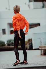 Image showing Fit attractive woman in sportswear stretching one leg before jogging on the footpath outdoor in summer among greenery. Workout, sport, activity, fitness, vacation and training concept.