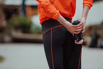 Image showing Fit attractive woman in sportswear stretching one leg before jogging on the footpath outdoor in summer among greenery. Workout, sport, activity, fitness, vacation and training concept.