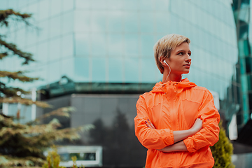 Image showing a woman in a sports outfit is resting in a city environment after a hard morning workout while using noiseless headphones