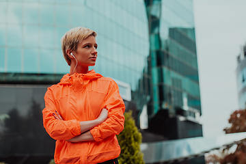 Image showing a woman in a sports outfit is resting in a city environment after a hard morning workout while using noiseless headphones