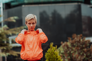 Image showing a woman in a sports outfit is resting in a city environment after a hard morning workout while using noiseless headphones