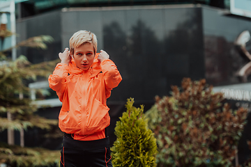 Image showing a woman in a sports outfit is resting in a city environment after a hard morning workout while using noiseless headphones