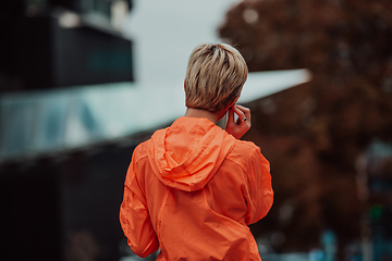 Image showing a woman in a sports outfit is resting in a city environment after a hard morning workout while using noiseless headphones