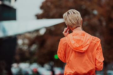 Image showing a woman in a sports outfit is resting in a city environment after a hard morning workout while using noiseless headphones