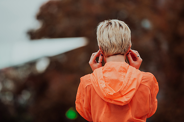 Image showing a woman in a sports outfit is resting in a city environment after a hard morning workout while using noiseless headphones