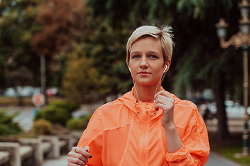 Image showing a woman in a sports outfit is resting in a city environment after a hard morning workout while using noiseless headphones