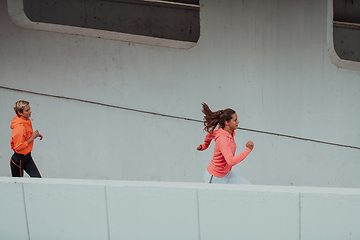 Image showing Two women in sports clothes running in a modern urban environment. The concept of a sporty and healthy lifestyle