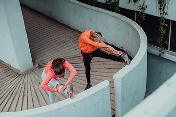 Image showing Two women warming up together and preparing for a morning run in an urban environment. Selective focus