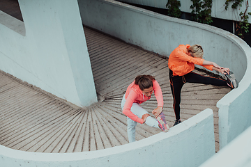 Image showing Two women warming up together and preparing for a morning run in an urban environment. Selective focus