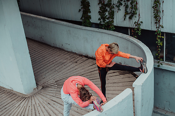 Image showing Two women warming up together and preparing for a morning run in an urban environment. Selective focus