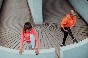 Image showing Two women warming up together and preparing for a morning run in an urban environment. Selective focus