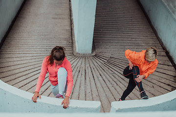 Image showing Two women warming up together and preparing for a morning run in an urban environment. Selective focus