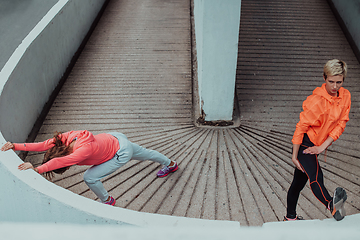 Image showing Two women warming up together and preparing for a morning run in an urban environment. Selective focus