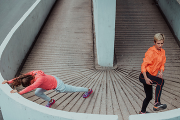 Image showing Two women warming up together and preparing for a morning run in an urban environment. Selective focus