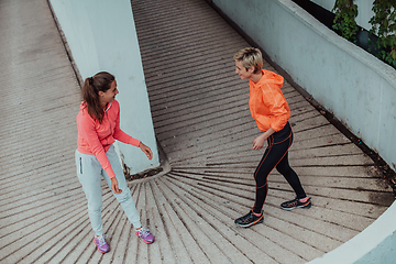 Image showing Two women warming up together and preparing for a morning run in an urban environment. Selective focus