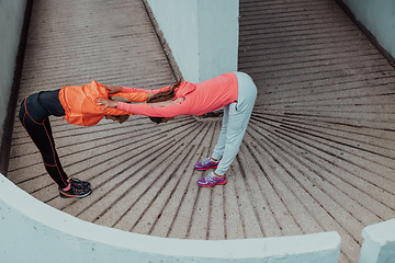 Image showing Two women warming up together and preparing for a morning run in an urban environment. Selective focus