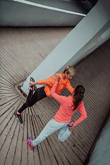 Image showing Two women warming up together and preparing for a morning run in an urban environment. Selective focus